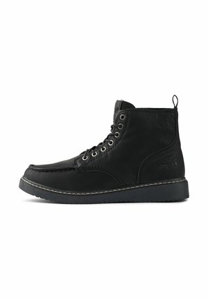 Botas de media caña de cuero negro con cordones, ojales plateados y una lengüeta trasera. Presentan un contraste de costura clara a lo largo de la suela.