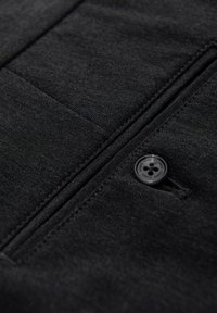 Zwart textiel met textuur, met een genaaide zak en een zwarte knop. Het ontwerp bevat strakke lijnen en subtiele stikdetails.