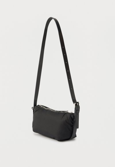 Μαύρη τσάντα ώμου με ρυθμιζόμενο λουρί και κλείσιμο με φερμουάρ, παρουσιάζεται σε απλό φωτεινό φόντο.