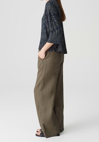 Blusa a righe navy con maniche a tre quarti, abbinata a pantaloni a gamba larga di un verde oliva chiaro. Entrambi realizzati in tessuto testurizzato e traspirante.