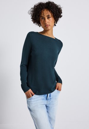 Teal lichtgewicht sweater met lange mouwen, een bootnek, geribbelde manchetten en zoom. Gecombineerd met lichtblauwe tapered jeans.