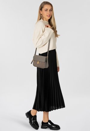 Maglione beige lavorato a maglia, gonna midi plissettata nera e scarpe in pelle lucida nera. Accessoriato con una borsa a tracolla marrone con hardware dorato.
