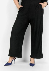 Pantalons larges noirs avec un motif zigzag texturé, dotés de poches latérales. Assortis à des escarpins bleus à bout pointu.