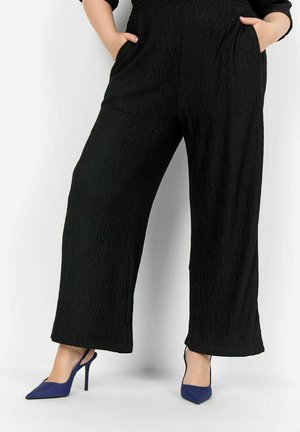 Pantaloni neri a gamba larga con un motivo zigzag testurizzato, dotati di tasche laterali. Abbinati a tacchi blu a punta.