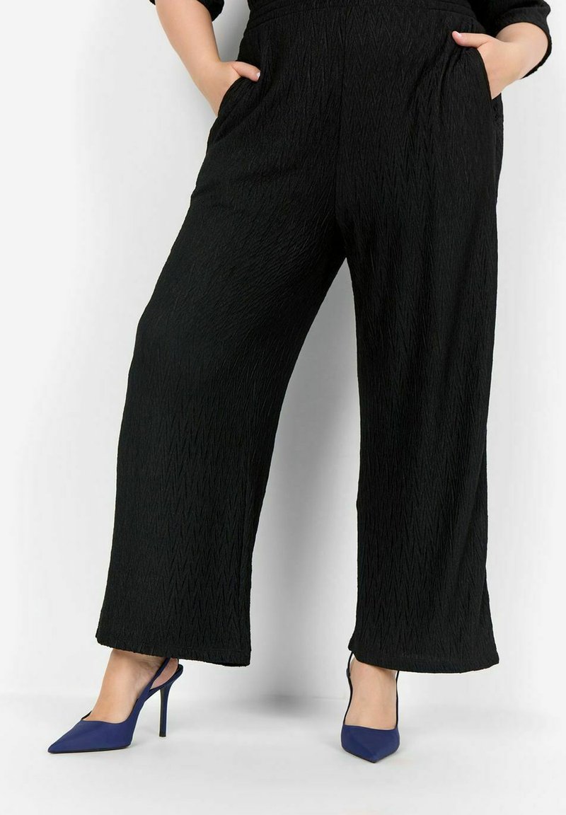 Pantalons larges noirs avec un motif zigzag texturé, dotés de poches latérales. Assortis à des escarpins bleus à bout pointu.