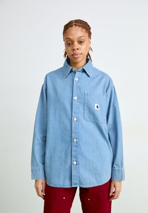 Svetlo modra denim srajca s gumbi in žepom na prsih, s srebrnimi gumbi in sproščenim krojem, v kombinaciji z rdečimi hlačami.