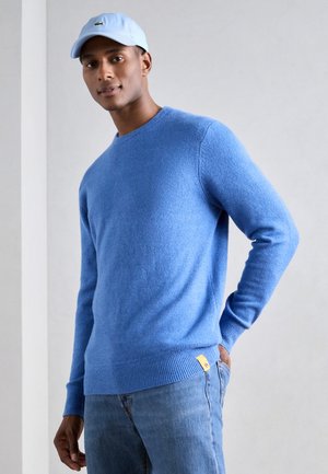 Light blue sweater made of soft knit material with a round neckline and ribbed cuffs, paired with blue denim jeans featuring a small logo tag.