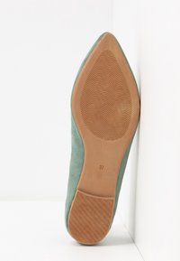 Chaussure en daim vert à bout pointu avec un talon fin et effilé. La semelle est en caoutchouc marron avec des rainures texturées, marquée de la taille 37.
