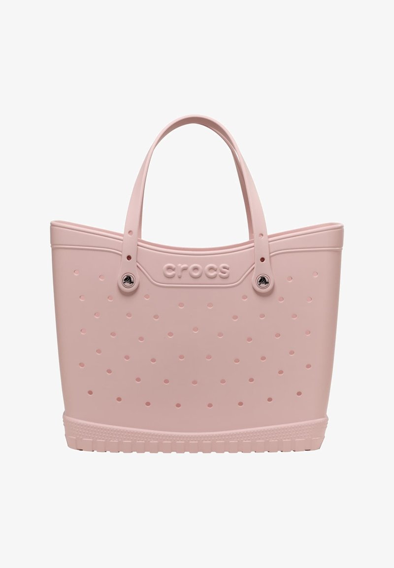 Hellrosa Crocs Tragetasche mit perforierten Löchern, doppelten Griffen und einer strukturierten Basis für das Tragen und den Freizeitgebrauch.