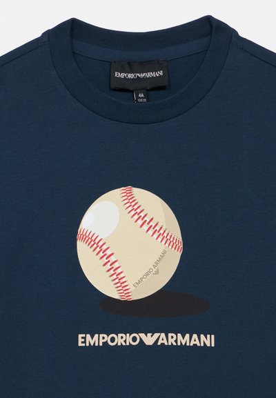 Μπλε βαμβακερό T-shirt σε ναυτικό μπλε, με γραφικό απεικόνιση μπέιζμπολ με κόκκινα ραφές και εκρού φόντο, με την επιγραφή "EMPORIO ARMANI" κάτω από αυτό.