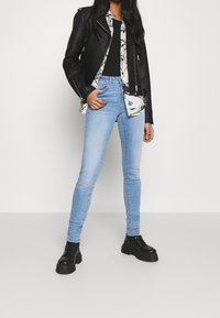 Svart läderbikerjacka över en blommig skjorta, matchad med ljusblå skinny jeans och svarta kraftiga stövlar. Enkel, åtsittande silhuett.