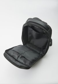 Borsa in tessuto nero con apertura zip, dotata di un compartimento imbottito e rivestimento interno liscio e testurizzato. Cinghia laterale.