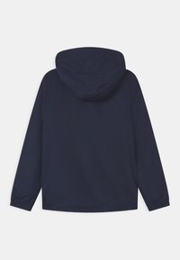 Námořnická modrá větrovka s kapucí, hladká textura, elastické manžety a jednoduchý design; pohled zezadu, bez viditelných detailů nebo vzorů.