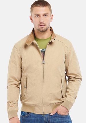 Lichtbeige bomberjack met een corduroy kraag, voorzakken en geribbelde manchetten. Gemaakt over een groene t-shirt, gepresenteerd tegen een witte achtergrond.