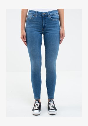 Kárované vysoké, úzké modré džíny s hladkým denimovým texturem a designem s pěti kapsami, doplněné černobílými šněrovacími teniskami.