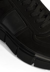 Schwarzer Sneaker mit einem strukturierten Lederoberteil, gepolstertem Zungenbereich und dicke, langlebige Sohle. Inklusive schwarzer Schnürsenkel und glatten Akzenten.