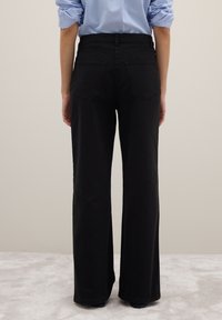 Pantaloni neri a gamba larga in denim, caratterizzati da vita alta, due tasche posteriori e un design pulito e minimalista.