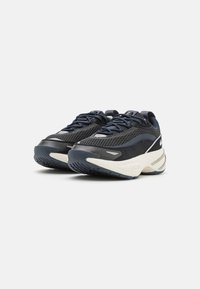 Baskets en mesh et suède noires et marine avec une semelle en caoutchouc blanc épaisse, présentant des lacets bleus et un logo sur la languette et le côté.