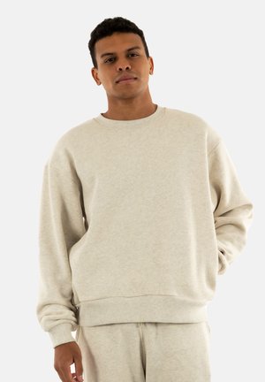Sudadera beige clara hecha de tejido suave, con cuello redondo, puños y cinturilla acanalados, con un corte relajado y mangas largas.