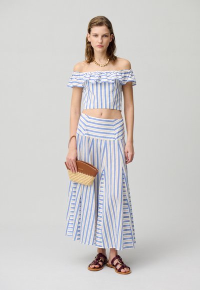 Completo a righe composto da un top corto senza spalle e una gonna alta in vita, nei colori blu e bianco. Include una borsa intrecciata e sandali.