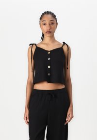 Svart cropped topp med justerbare knytetråder, v-hals og fem dekorative knapper foran. Mykt stoff og avslappet passform.