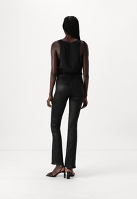 Black sleeveless top, fitted black jeans with flared legs, and strappy black heels. Smooth texture, minimalistic design, no patterns or accents.