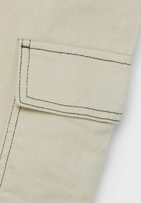 Bežová tkanina s vertikální žebrovanou texturou, s přímou kapsou s kontrastním tmavým prošíváním. Jednoduchý, funkční design.