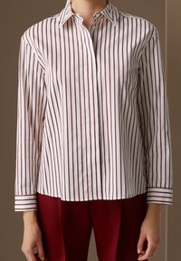 Camisa blanca de botones con estrechas rayas verticales en burdeos, de manga larga, con cuello clásico y puños a rayas, combinada con pantalones burdeos.