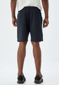 Marinblå idrottsshorts med elastisk midja, sidfickor och avslappnad passform, med en mjuk textur och diskret design.