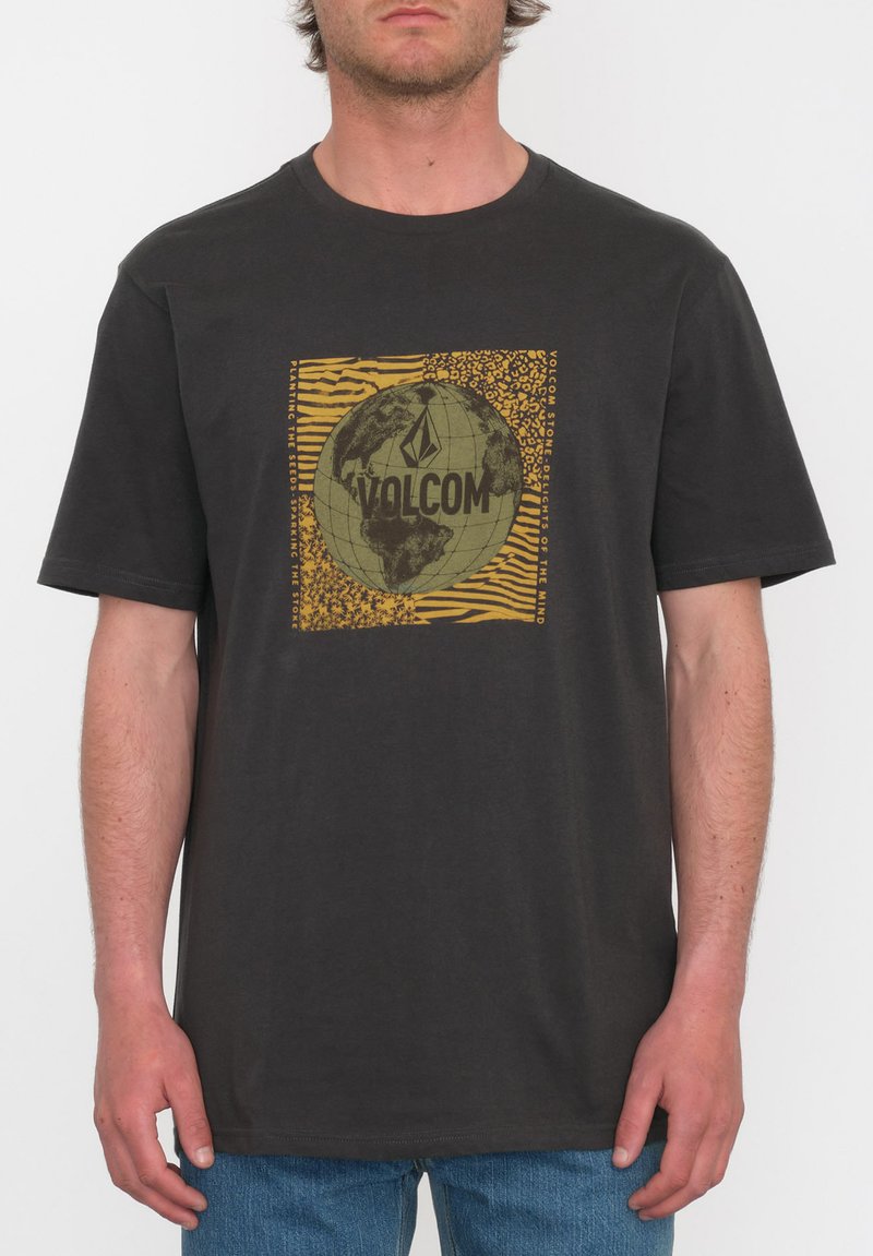 Camiseta de algodón negra con un gráfico de un globo multicolor y el logo de "Volcom", sobre un fondo con un patrón geométrico.