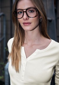 Wit geribd henley shirt met een knoopsluiting, gecombineerd met grote brillen met schildpadmotief en stijl, lichtbruin haar.