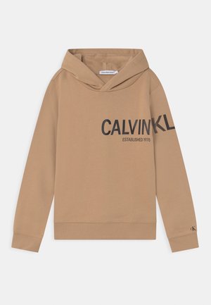 Sweat-shirt à capuche beige avec une texture douce. Il présente un grand graphique en texte noir et des poignets et un ourlet côtelés. Étiquette visible à l'intérieur de la capuche.