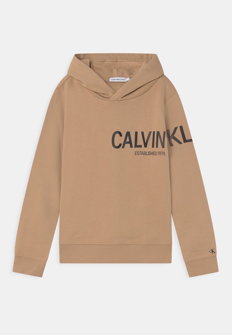 Tan hoodie med mjuk textur. Den har en stor svart textgrafik och ribbade ärmslut och nederkant. Lappen är synlig inuti huvan.
