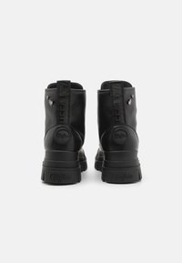 Botas de tobillo de cuero negro con un acabado texturizado, que cuentan con una suela resistente, acentos en relieve y herrajes decorativos en forma de corazón.