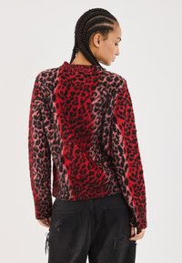 Suéter de leopardo en rojo y negro con mangas largas y cuello redondo, con una textura suave y un corte relajado.