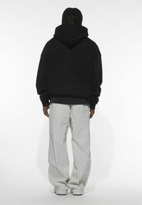 Sudadera negra con capucha de corte holgado, combinada con pantalones cargo gris claro que cuentan con grandes bolsillos y puños elásticos.