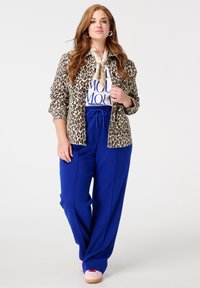 Jas met luipaardprint, wit T-shirt met blauwe tekst, blauwe wijde broek en roze schoenen. De sjaal is crème-kleurig met een satijnen afwerking.
