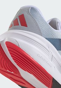 Baskets de sport grises avec des accents rouges et une tige texturée. La semelle blanche présente une bande de roulement prononcée avec le logo "CLOUDFOAM".
