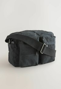 Sort canvas taske med lynlåslukning, justerbar nylonrem, to forlommer, rektangulær form og struktureret overflade.
