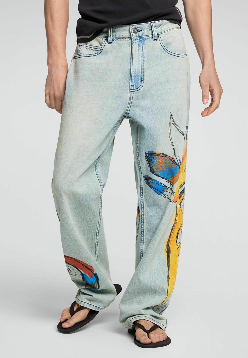 Lyseblå løse jeans med farverige abstrakte blomsterprint, båret med sorte klipklapper og en sort skjorte.