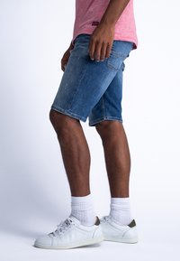 Shorts de mezclilla en tonos de azul claro a medio con una textura deslavada, con un corte recto y bolsillos laterales, combinados con zapatillas blancas y calcetines.