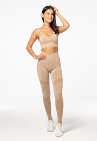 Gaiši brūns sporta krūšturis un legingi, kas izgatavoti no faktūras auduma, ar pieguļošu dizainu, dekorēti ar acs akcentiem un augstu jostasvietu.