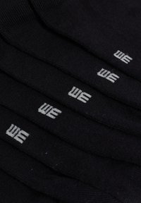 Črne nogavice zložene v kup, z vtkanim belim logotipom "WE" na vsakem paru. Material deluje mehak z gladko teksturo.