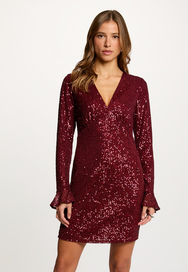 Viininpunainen paljettimekko syvällä V-pääntiellä, pitkät hihat, joissa levenevät kalvosimet, ja vartaloa myötäilevä siluetti. Kimmeltävä pinta kauttaaltaan.