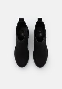 Pár černých volnočasových kotníkových bot se zaoblenými špičkami a poutky na stažení, z pohledu shora na bílém pozadí.