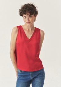 Rode mouwloze top met een V-hals ontwerp, gemaakt van soepel stof. Gecombineerd met blauwe jeans, wat een casual en aangesloten silhouette toont.