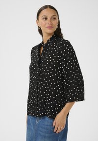 Black button-up shirt with white polka dots, lightweight fabric, relaxed fit, 3/4 sleeves, small collar, and a buttoned front placket.
