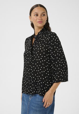 Chemise noire à boutons avec des pois blancs, en tissu léger, coupe décontractée, manches 3/4, petit col et patte de boutonnage à l'avant.