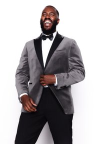 Veste de smoking en velours gris avec revers en satin noir à pointe, portée sur une chemise blanche avec un nœud papillon, associée à un pantalon noir.