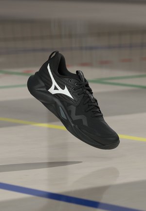 Czarny but sportowy z białym logo unoszący się nad podłogą kortu sportowego oznaczoną niebieskimi, zielonymi i żółtymi liniami.